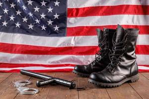 handcuffs, black boots and police nightstick near US flag on wooden surface photo