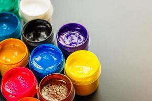 close-up background of opened small gouache paint jars on black surface photo