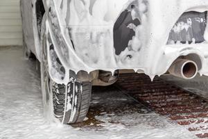 a fossil fuel car covered by soap foam while washing indoors - close-up low angle view from back with selective focus photo