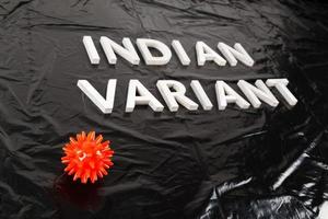 words indian variant laid with silver metal letters on crumpled black plastic bag background with small virus model photo