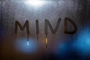 the word mind written on night wet window glass close-up with blurred background photo