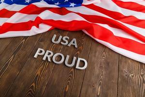 words USA proud laid with silver metal letters on brown wooden surface with flag of United States of America photo