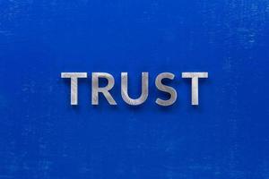 the word trust laid with silver metal characters on blue painted wooden board in central flat lay composition photo