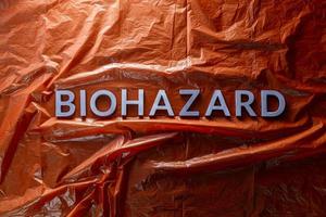 the word biohazard laid with silver letters on red crumpled plastic film background in flat lay composition at center photo