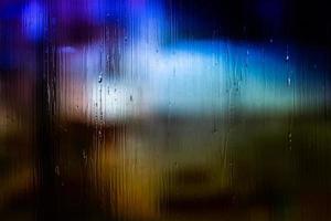 un fondo abstracto luces de la calle de noche bokeh a través de vidrio húmedo con gotas de agua, primer plano con enfoque selectivo foto