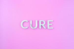 the word cure laid with thick aluminium letters on pink background photo