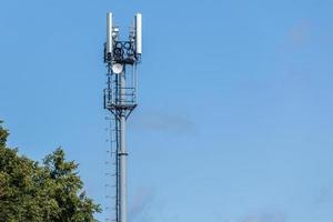 torre de telecomunicaciones de tubería gris con la parte superior del árbol verde en el cielo azul con fondo de nubes foto