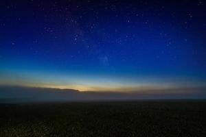 Foggy night field with starry night sky and afterglow horizon gradient photo
