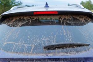 Dirty car glass with wiper and third brake light, rear window covered with a layer of dust. photo