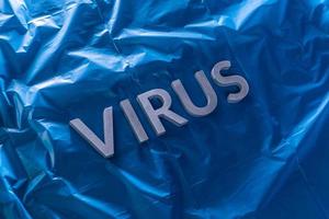 the word virus laid with silver metal letters on crumpled blue plastic film with dramatic light photo