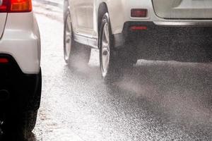 el agua de lluvia salpica el flujo de las ruedas de los autos blancos que se mueven rápido en la ciudad a la luz del día con enfoque selectivo foto