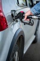 hand in jeans jacket refueling gray metallic car on gas station - closeup with selective focus - vertical composition photo
