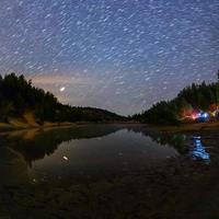 pequeño lago bajo las estrellas por la noche con rieles cortos y camping en verano foto