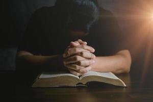 mano de persona de oración en fondo negro. la mujer católica cristiana está rezando a dios en la oscuridad en la iglesia. chica cree y fe en jesucristo. la religión de cristo y el cristianismo adoran o rezan concepto. foto