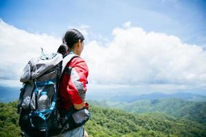 Young person hiking female standing on top rock, Backpack woman looking at beautiful mountain valley at sunlight in summer, Landscape with sport girl, high hills, forest, sky. Travel and tourism. photo