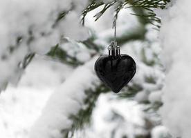 Christmas background with Christmas tree toy black heart on snow covered pine branch in winter forest, copy space photo