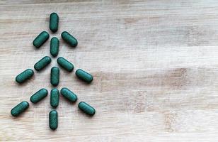 Pills of chlorella, spirulina or barley grass in the shape of a herringbone or christmas tree on a light wooden background with a copy space photo