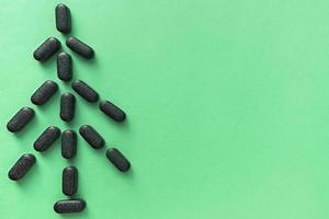 Pills of chlorella, spirulina or barley grass in the shape of a herringbone or christmas tree on light green background with a copy space photo