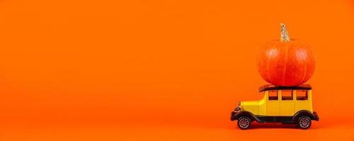 Retro toy car with a pumpkin on an orange background. Halloween and autumn harvest concept. photo