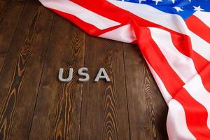 the word USA laid with silver metal letters on wooden board surface with crumpled flag of United States of America upper right side photo