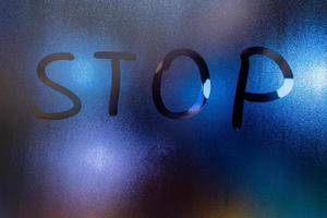 the word stop written on night wet window glass close-up with blurred background photo