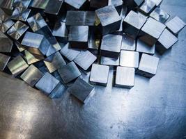 pile of small machined shiny steel cubes on metal surface photo