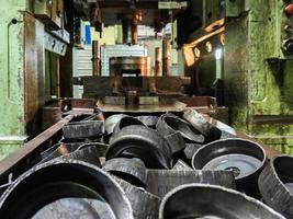 pile of stamped thick sheet black metal round parts after a hood operation in front of forming press with die tooling photo