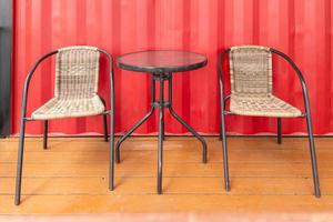 two wicker chairs and glass table near red wall of roadside cafe, empty photo