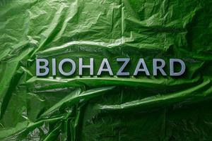 the word biohazard laid with silver letters on green crumpled plastic film background in flat lay composition at center photo