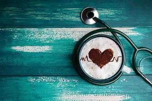 World Health Day. Health Care for Coffee Lover and Heart Disease Concept. Latte Art by Cinnamon on Top as Heart Shape and Pulse Beat Rate. Hot Coffee Cup Lay on Table inside Stethoscope. Top View