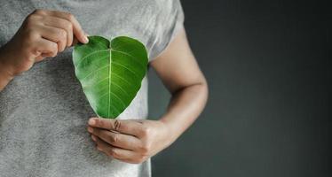 Green Energy, Renewable and Sustainable Resources. Environmental and Ecology Care Concept. Close up of Hand Holding a Heart Shape Green Leaf on Chest photo