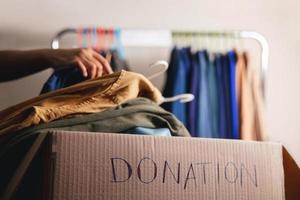 Donation Concept. Preparing Used Old Clothes from Wardrobe Rack into a Donate Box. Focus on Text photo