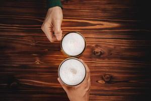 un par de hombres y mujeres o amigos sosteniendo un vaso de cerveza para celebrar en un restaurante o bar, para el oktoberfest o cualquier concepto de evento alegre, vista superior en una mesa de madera foto