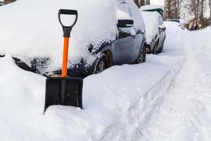Plastic snow shovel in front of snow-covered car at winter morning photo