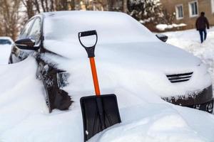 plastic snow shovel in front of snow-covered car at sunny winter morning photo