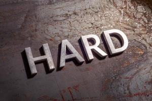 the word hard laid with silver metal letters on rusted burnt iron flat surface background photo