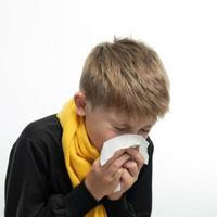 A child blows his nose into a napkin, children's seasonal diseases, a boy wrapped in a scarf. photo