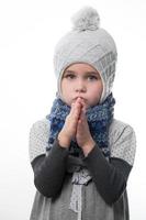 niña molesta con un sombrero gris envuelto en una bufanda sobre un fondo blanco, esperando el frío invierno. foto