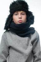 retrato de un niño con un sombrero de invierno con orejeras y una bufanda de punto sobre un fondo blanco. foto