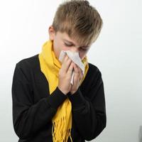 A boy wrapped in a scarf has a runny nose and blows his nose into a napkin. photo