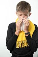 A boy wrapped in a scarf has a runny nose and blows his nose into a napkin. photo