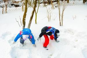 niños felices jugando bolas de nieve, dos hermanos disfrutando de las vacaciones de invierno, juego enérgico en la nieve. foto