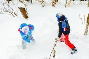happy children playing snowballs, two brothers enjoying winter vacation, energetic game in the snow. photo