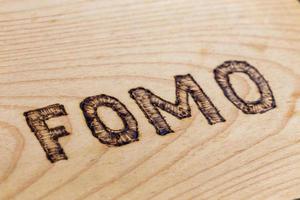 Abbreviation FOMO - fear of missing out - burnt by hand on flat wooden surface. Diagonal view with selective focus. photo