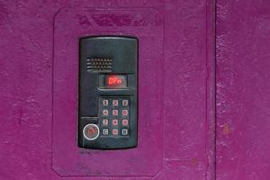An intercom on old painted pink steel surface with a keypad, digital display and rfid sensor for calling close-up photo