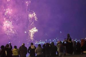 vista desde atrás a la gente con ropa de wark disparando fuegos artificiales por teléfono en la noche fría. foto