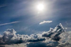 distant misty backlit cumulus and feather clouds near horizon closeup telephoto shot with sun. photo