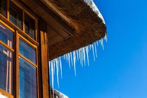 Icicles on roof corner of wooden house photo