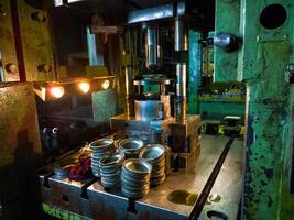 low tech stamping press producing round aliminium parts in dark environment photo