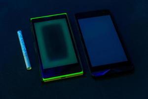 used phones and cigarette under UV light on black bckground with selective focus photo